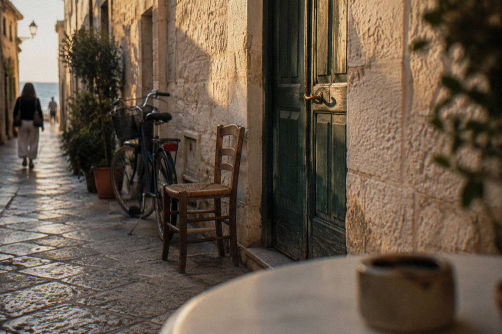 Faded green wooden door in a pale limestone wall with a chair and a bicycle beside it