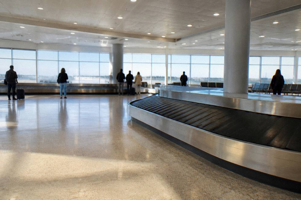 Baggage reclaim hall with an empty belt curving through and a few travellers watching far off