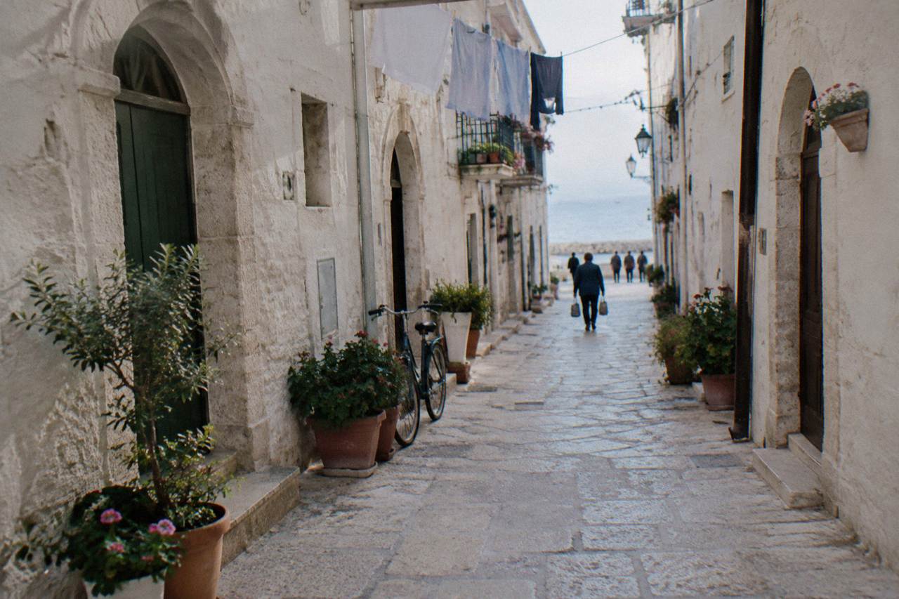Narrow whitewashed old town lane with arched doorways, flower pots, washing overhead and a leaning bicycle in soft morning light