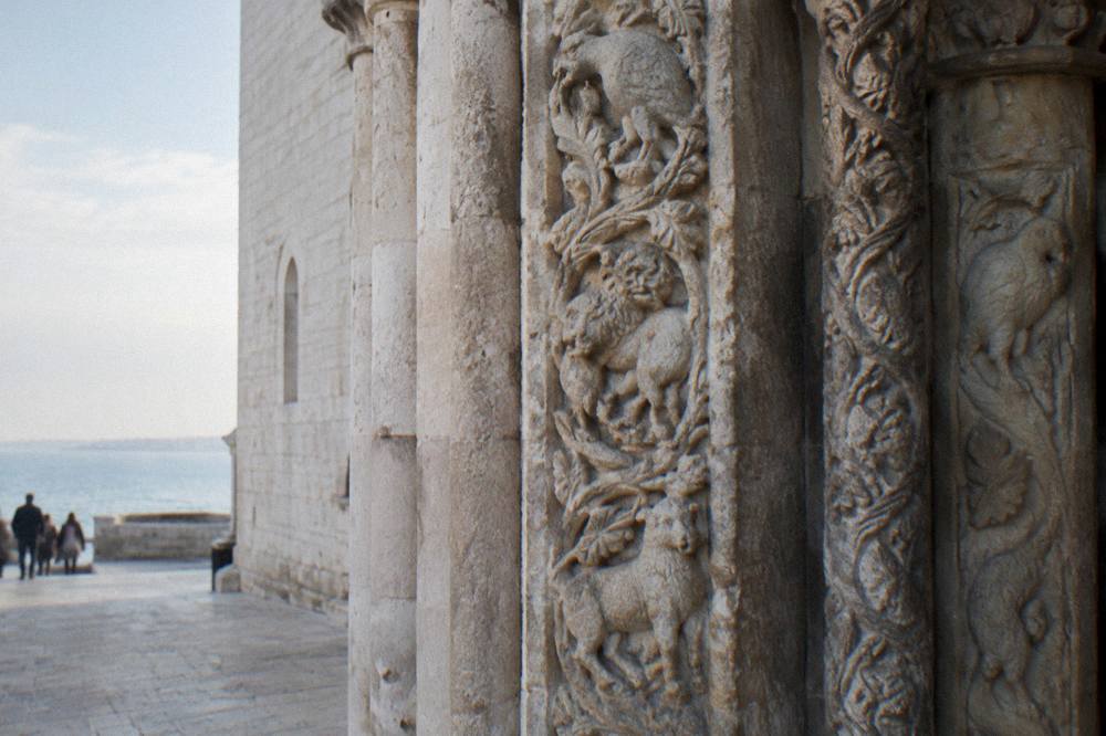 Weathered pale limestone carving of animals and foliage around a Romanesque church doorway in soft side light