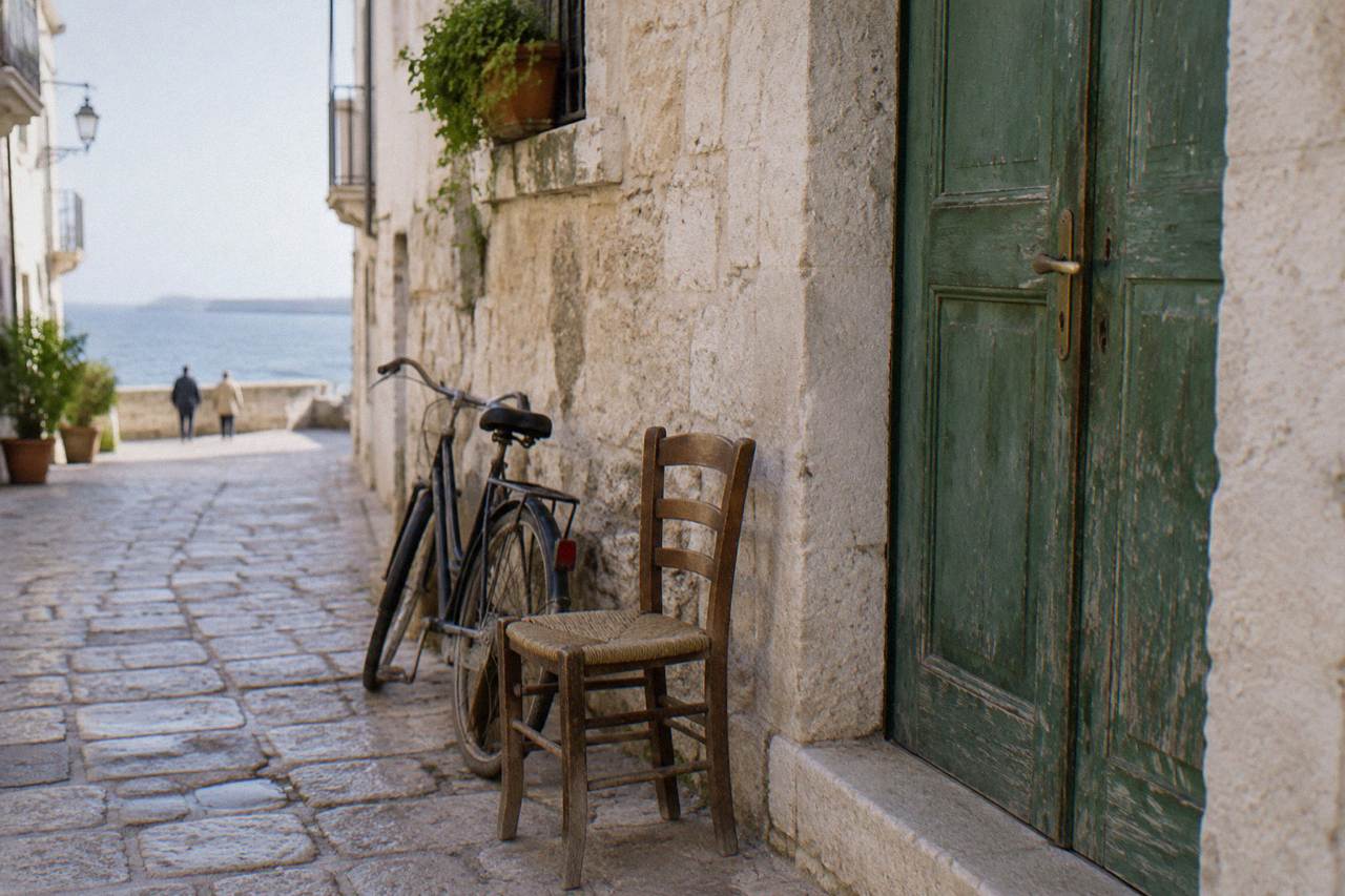Faded green wooden door in a pale limestone wall with a chair and a bicycle beside it