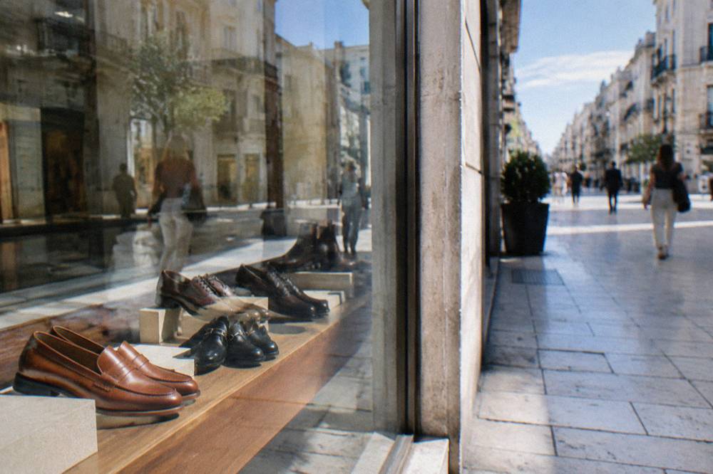 Shop window with leather shoes behind glass reflecting the street and a blurred passer-by