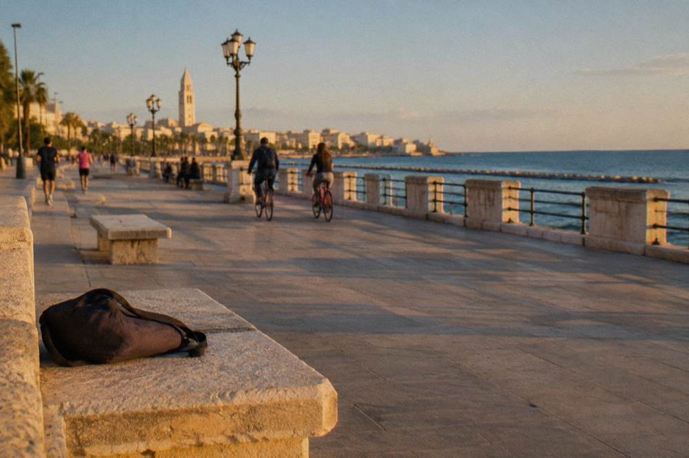 Wide paved seafront promenade with distant joggers and cyclists, benches and calm blue sea in late afternoon