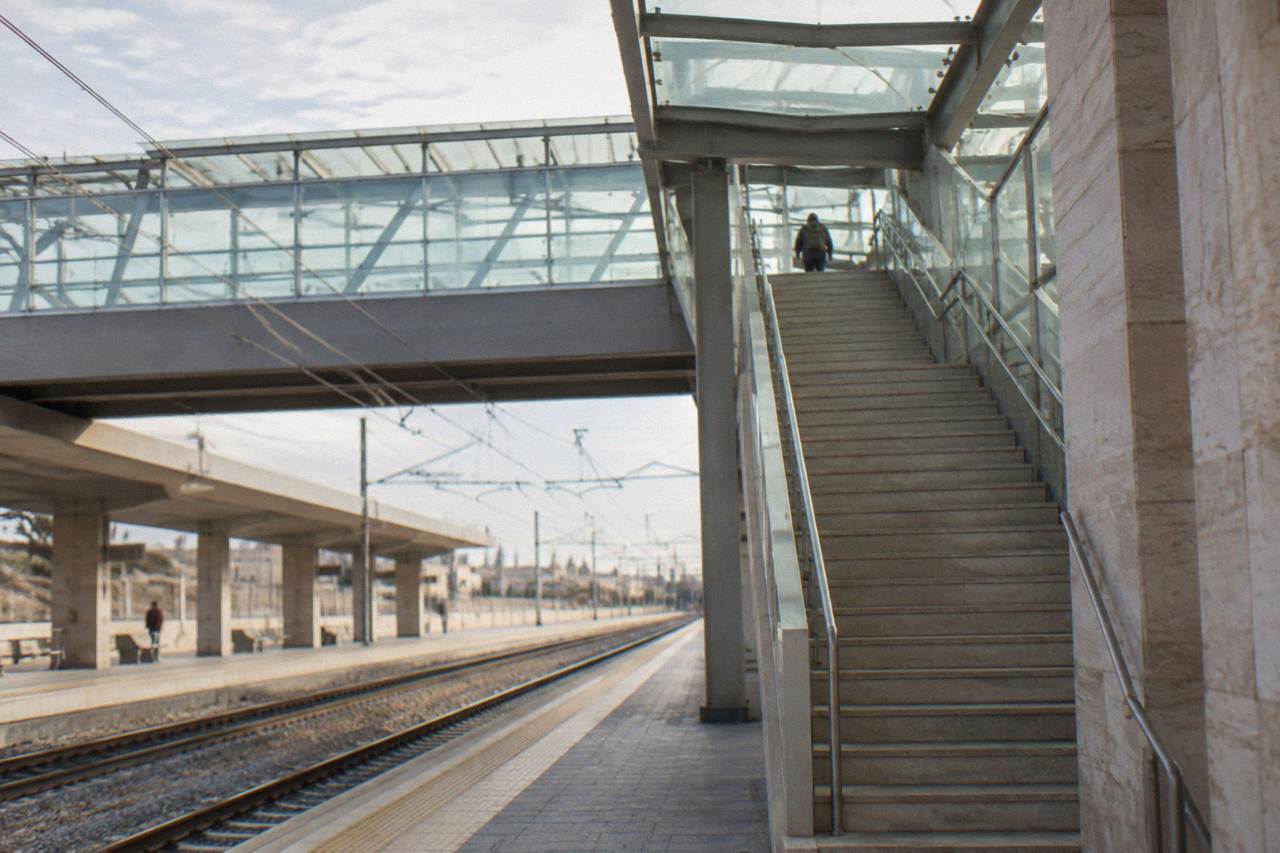 Station footbridge with stairs and a glass roof and a distant traveller with a rucksack