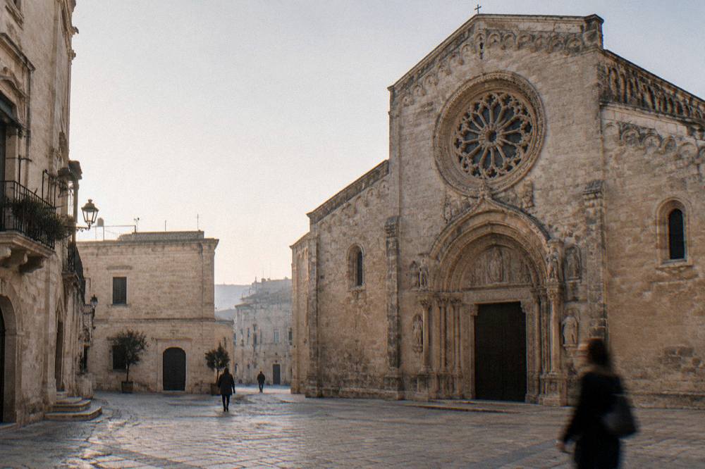 Romanesque cathedral in warm limestone with a carved rose window and portal on a small square