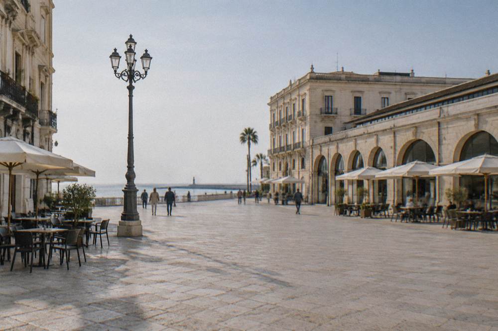 Broad open piazza beside a long low market hall with arched openings and outdoor cafe tables in bright morning