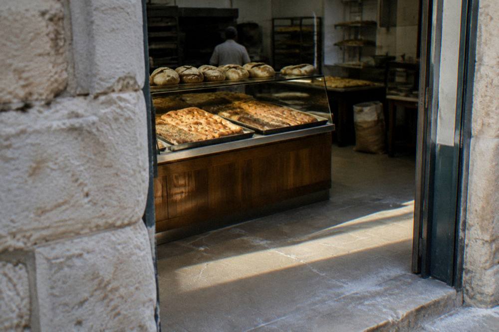 Neighbourhood bakery doorway with trays of golden focaccia and round loaves seen from the street