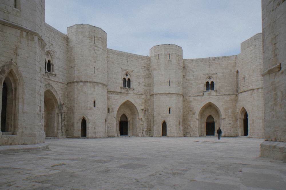Octagonal inner courtyard of a medieval castle with arched doorways in pale stone and a blue sky