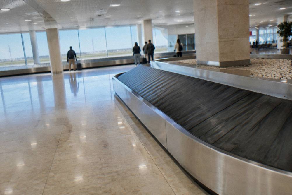Baggage reclaim hall with an empty belt curving through and a few travellers watching far off