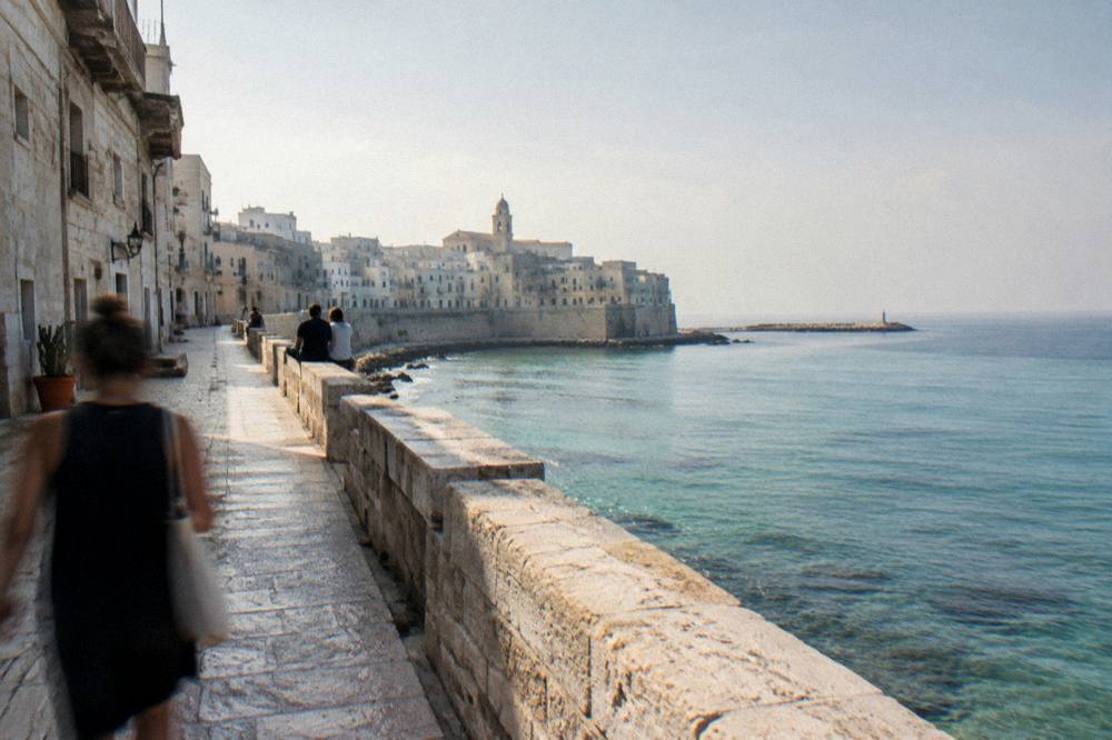 Sea promenade along an old town wall above calm turquoise water with distant people sitting on the wall