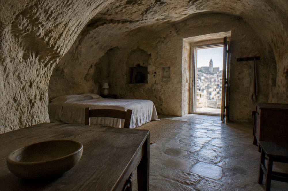 Inside a restored cave dwelling with an arched rock ceiling, a simple bed and a wooden table