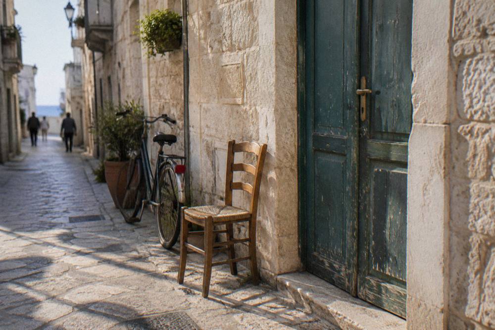 Faded green wooden door in a pale limestone wall with a chair and a bicycle beside it
