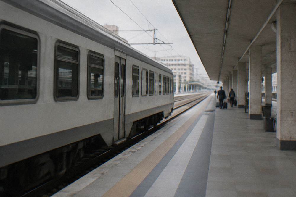 Regional train pulling into a station platform under a long canopy with a few distant waiting travellers