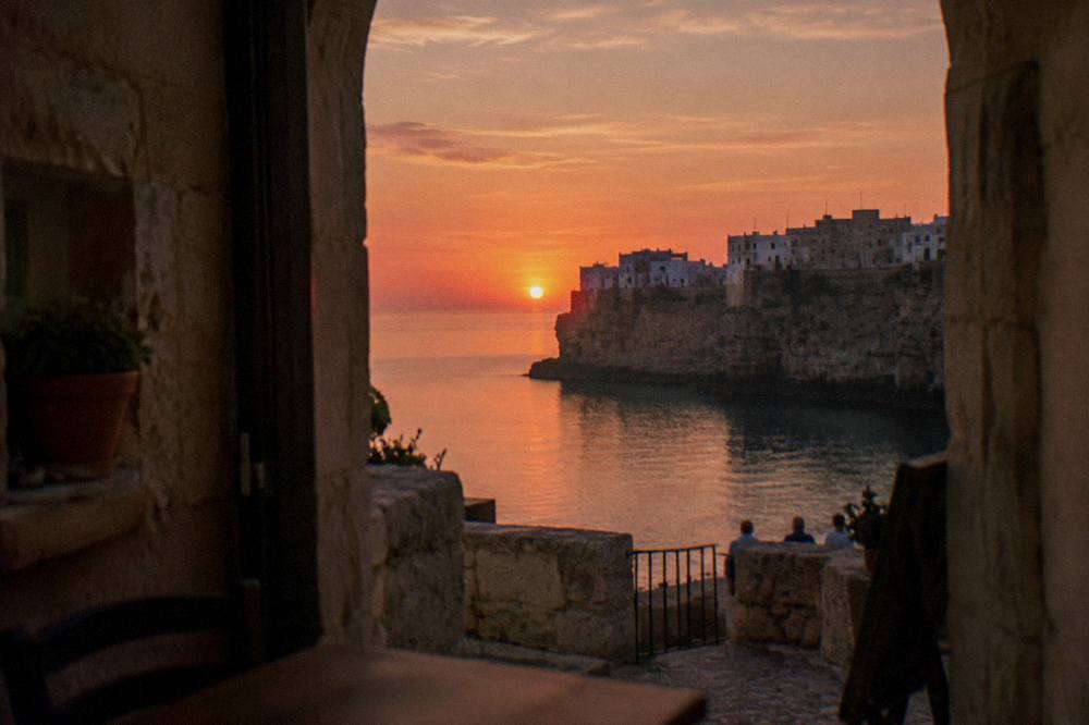 Cliff-top town in silhouette against a pink and orange sunset over a calm sea