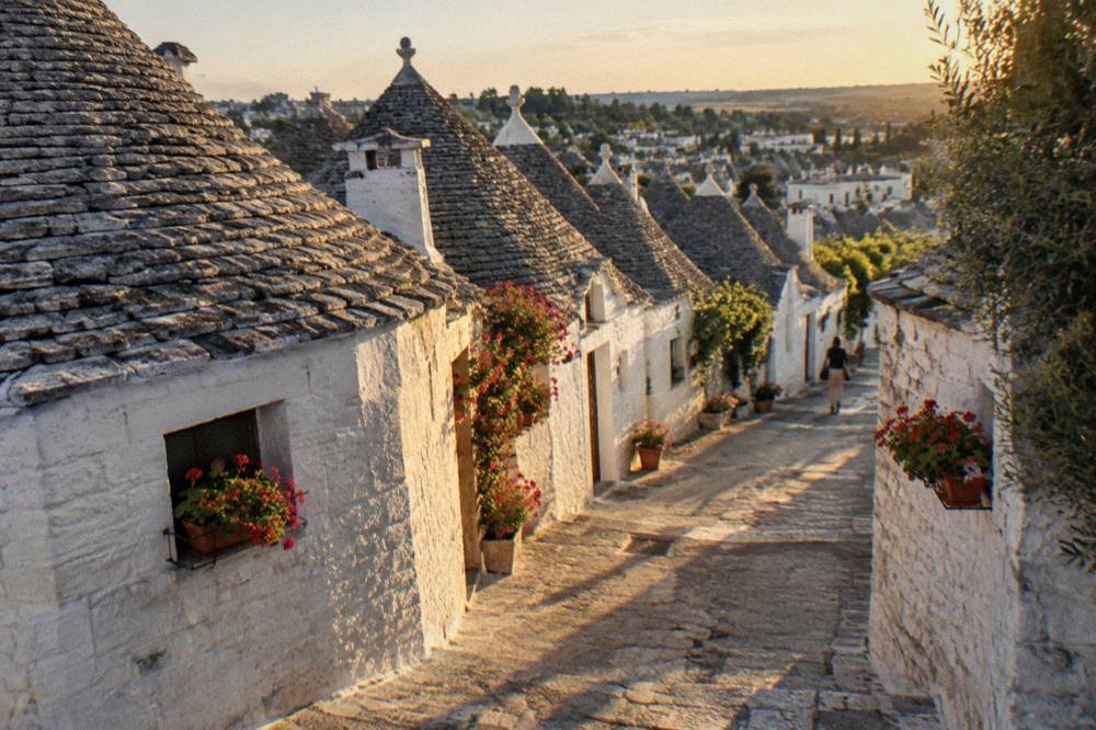 Quiet lane of conical-roofed houses at golden hour with long shadows and window boxes of geraniums