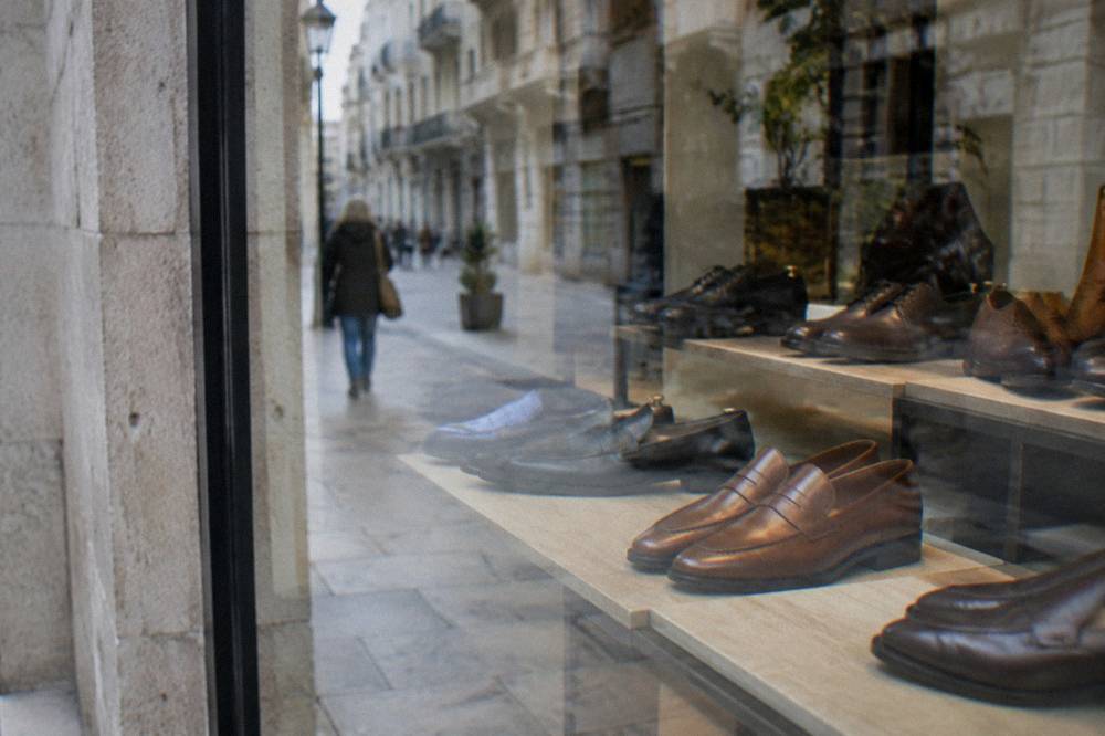 Shop window with leather shoes behind glass reflecting the street and a blurred passer-by