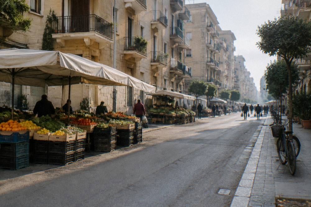 Residential street of apartment blocks with fruit and vegetable stalls under plain awnings and distant shoppers