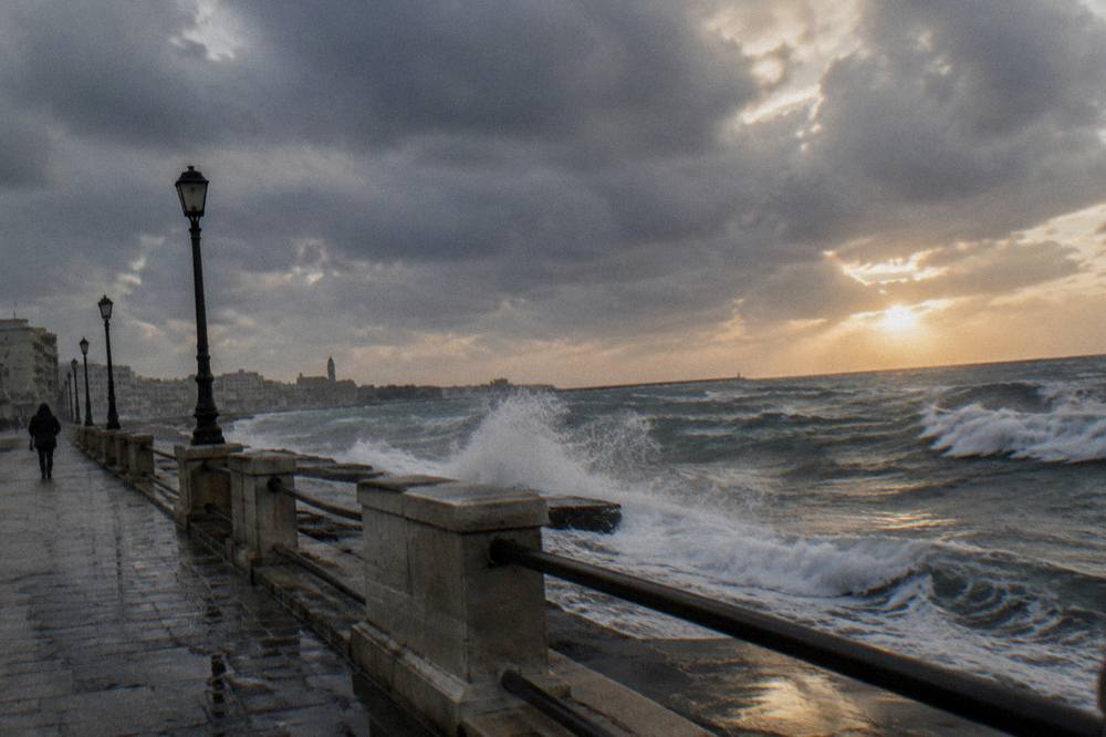 Grey winter sea with white-capped waves breaking against a seafront wall under a heavy sky