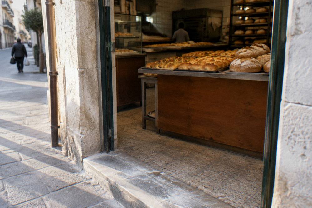 Neighbourhood bakery doorway with trays of golden focaccia and round loaves seen from the street