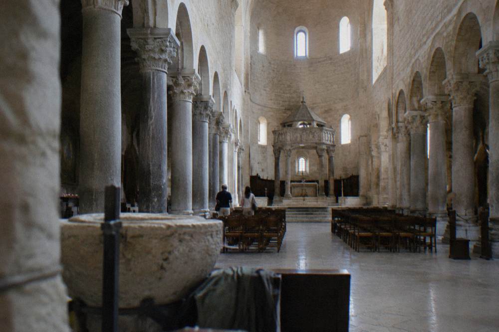 Long stone nave of a Romanesque basilica with simple columns and a raised sanctuary in soft window light