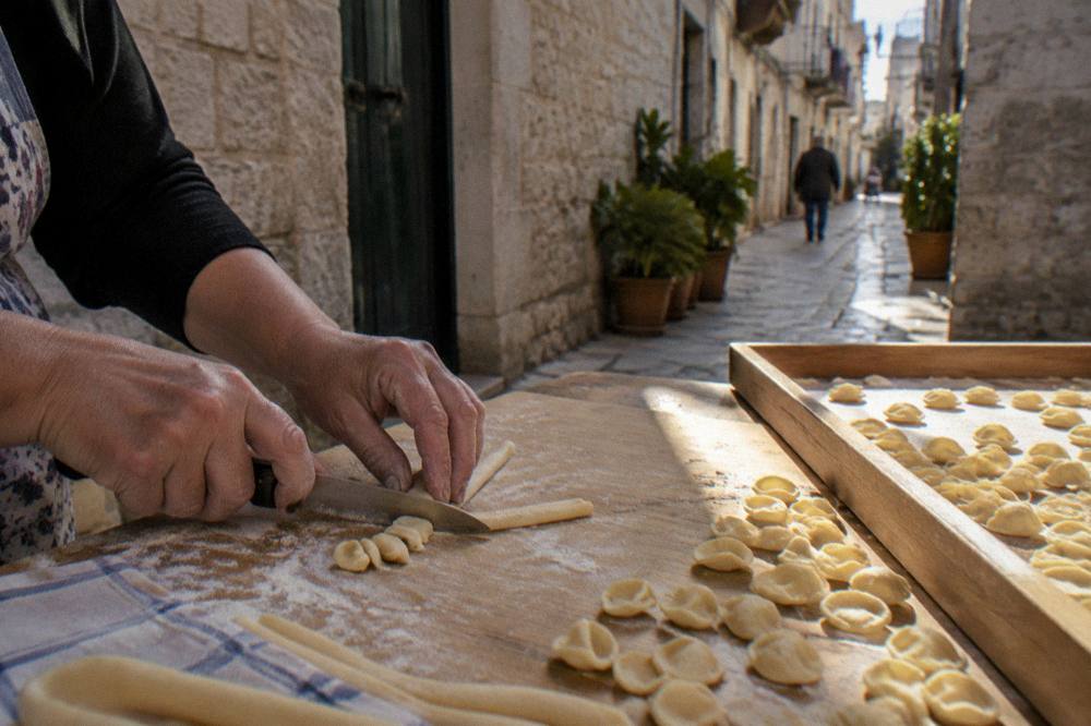 Floury hands drawing a small piece of dough across a board with a knife beside rows of finished pasta
