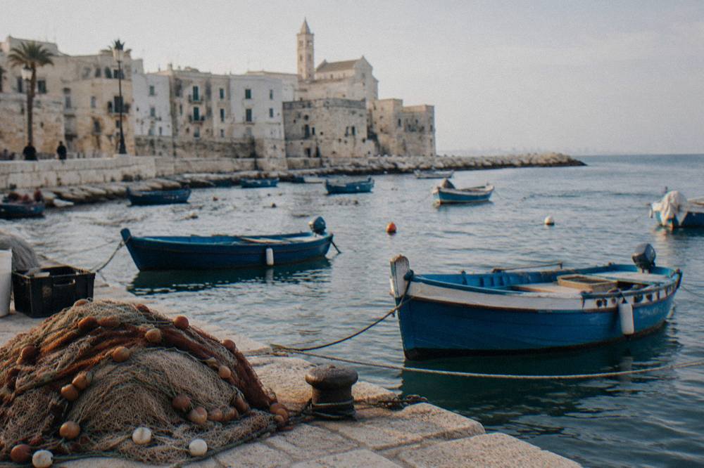 Small wooden fishing boats rocking at moorings with a net heap on the quay and pale old town walls behind