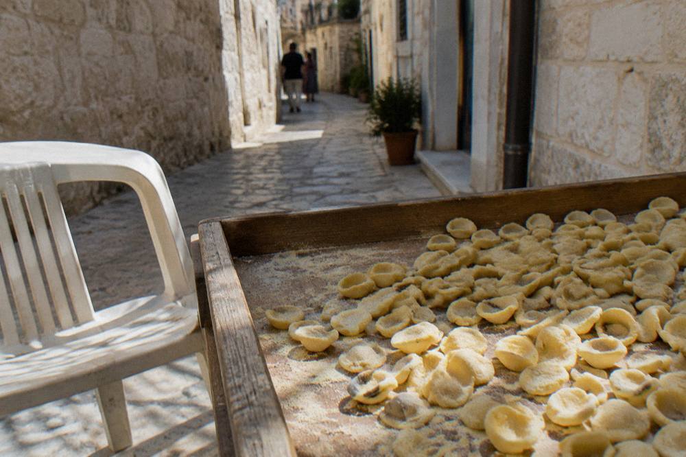 Tray of small ear-shaped orecchiette dusted with semolina on a wooden table beside a plastic chair