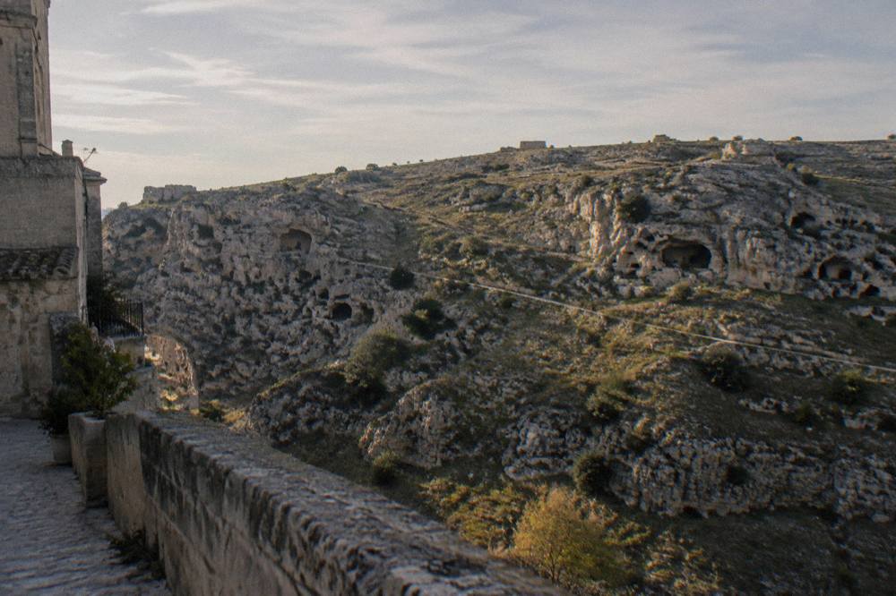 Rocky plateau across a ravine with scattered cave openings and sparse scrub in clear late light