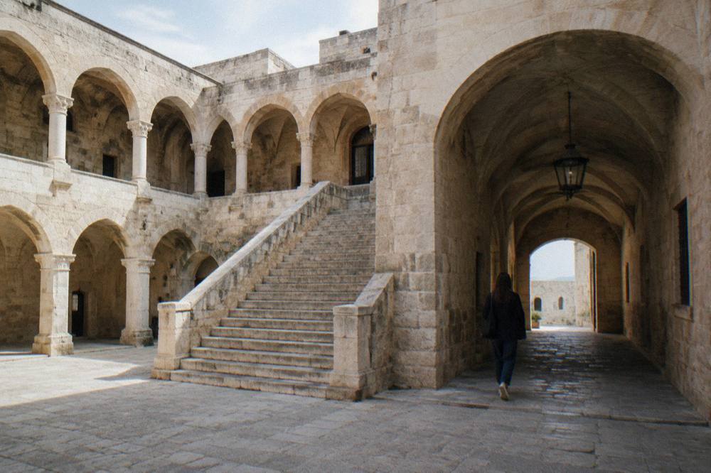 Inner courtyard of a medieval castle with a pale stone arcade, a broad staircase and a vaulted passage