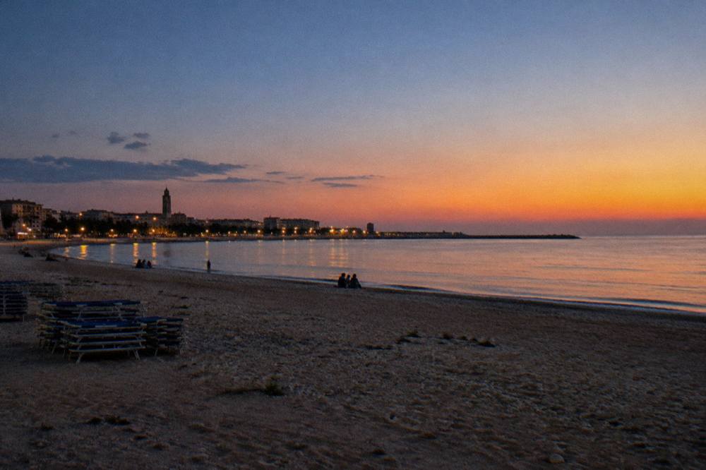City beach in the evening with distant people on the sand, stacked sunbeds and an almost still sea