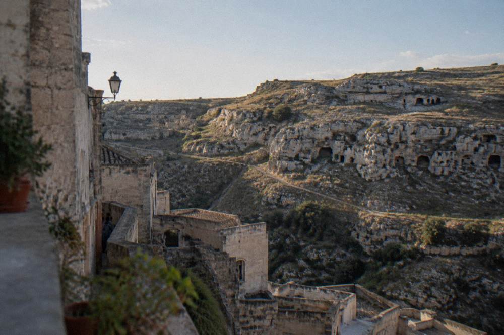 Rocky plateau across a ravine with scattered cave openings and sparse scrub in clear late light