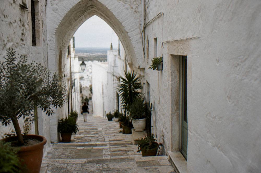 Steep whitewashed alley with stone steps, a pointed arch overhead and potted plants