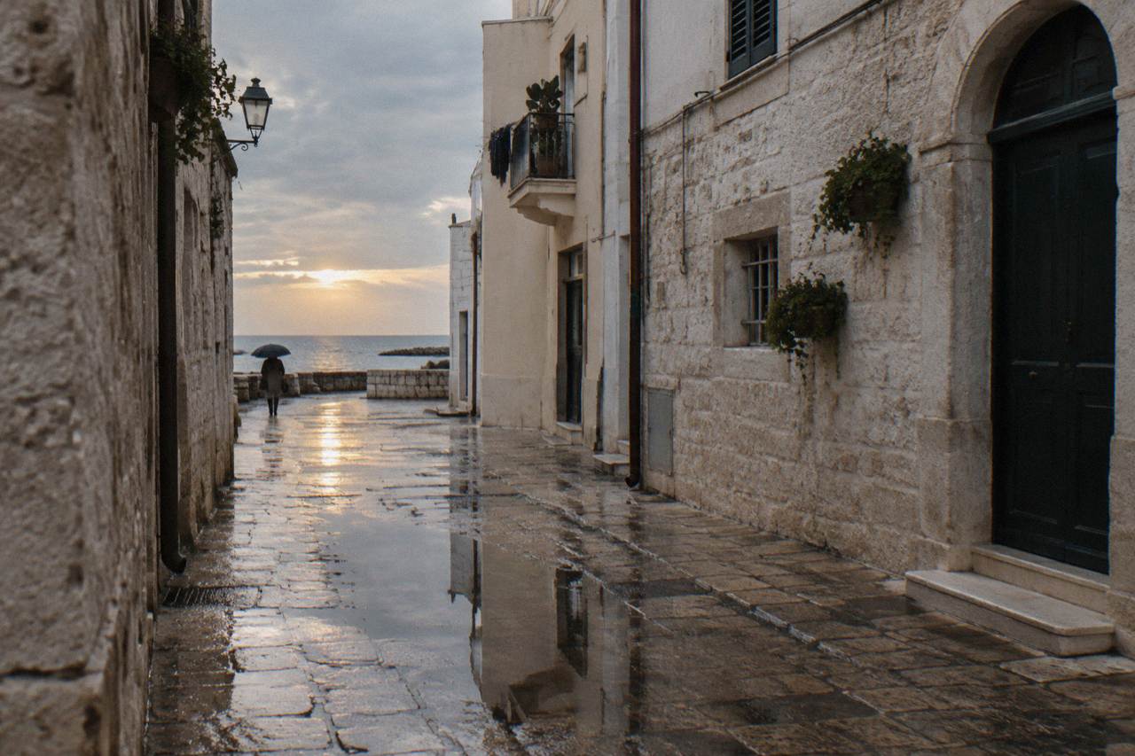 Wet limestone old town lane after rain with reflections in puddles and a distant person under an umbrella