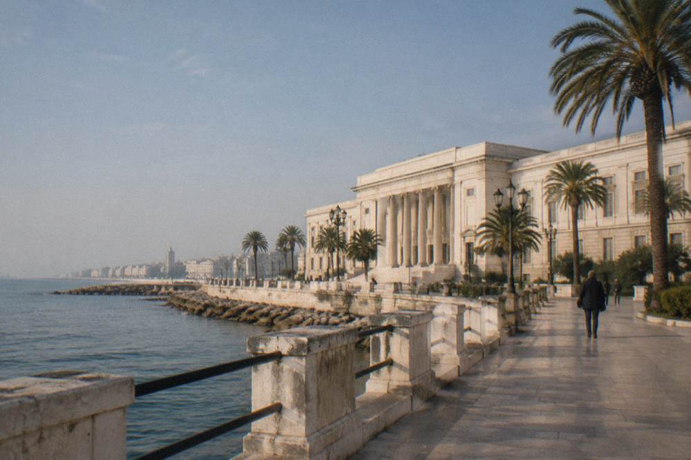Grand neoclassical seafront palace with a long cream facade, a central portico and palm trees