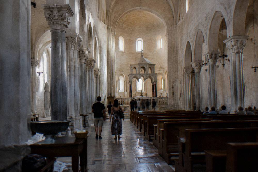 Long stone nave of a Romanesque basilica with simple columns and a raised sanctuary in soft window light