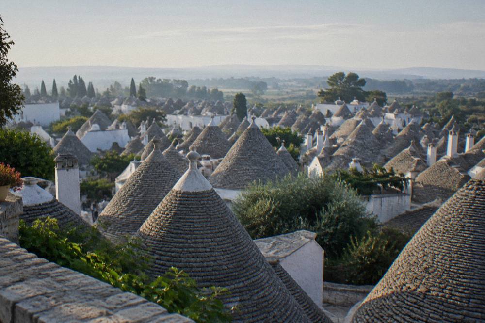 Wide view over a dense cluster of grey conical stone roofs from a raised belvedere