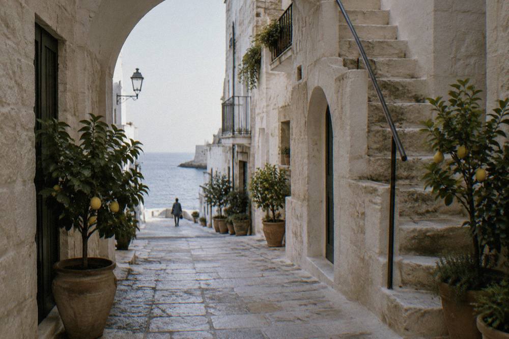 Narrow limestone lane with pale arches, a stone staircase and potted lemon trees in soft morning light