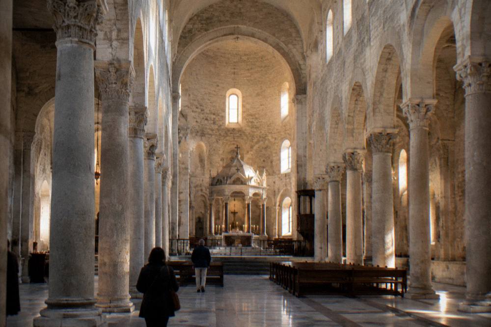Long stone nave of a Romanesque basilica with simple columns and a raised sanctuary in soft window light