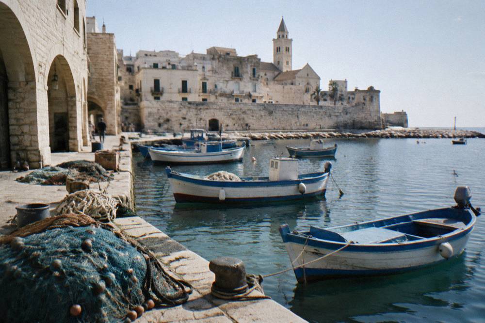 Small wooden fishing boats rocking at moorings with a net heap on the quay and pale old town walls behind