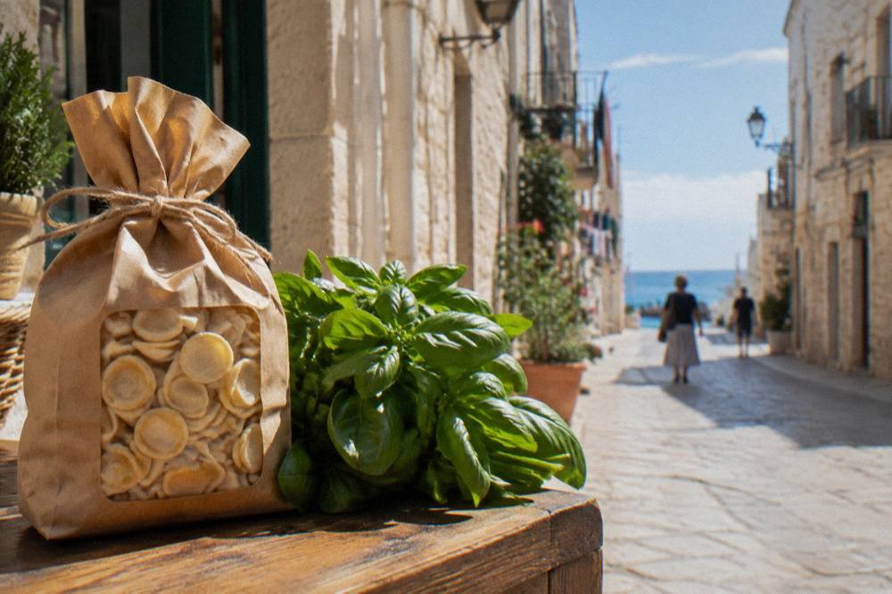 Paper bag of dried orecchiette tied with string on a wooden counter next to a bunch of basil