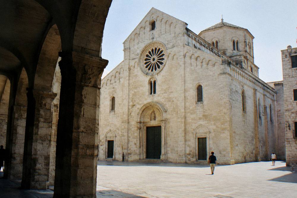 Romanesque cathedral of golden limestone with blind arcading, a wheel window and an octagonal drum dome above a small square